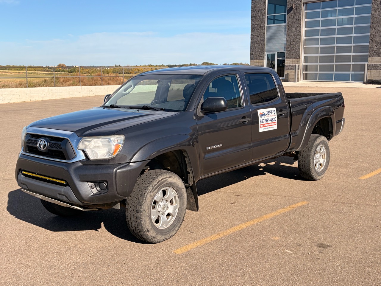 Jeff’s Junk Removal grey Toyota Tacoma with branded door magnet, viewed from the front and driver’s side